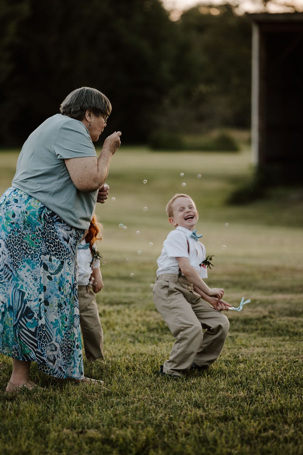 A joyful moment captured outdoors as bubbles float through the air on a grassy lawn at sunset.