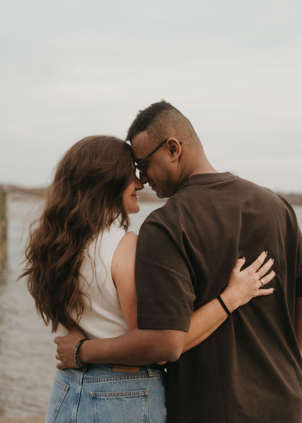 A couple embraces intimately by the water during a romantic sunset photoshoot.