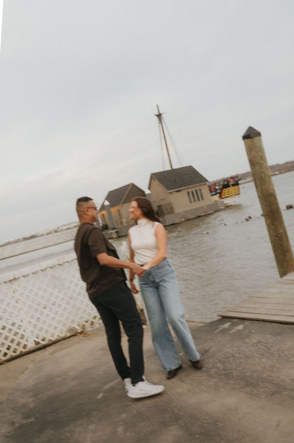 A couple walks together on a wooden dock by the water.