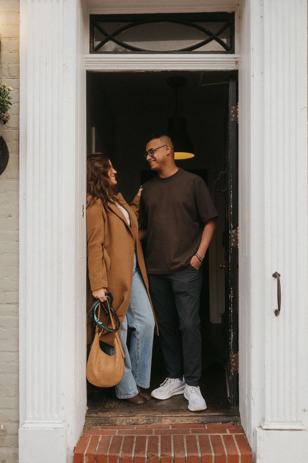 Couple standing in a white-columned doorway entrance of a brick building.