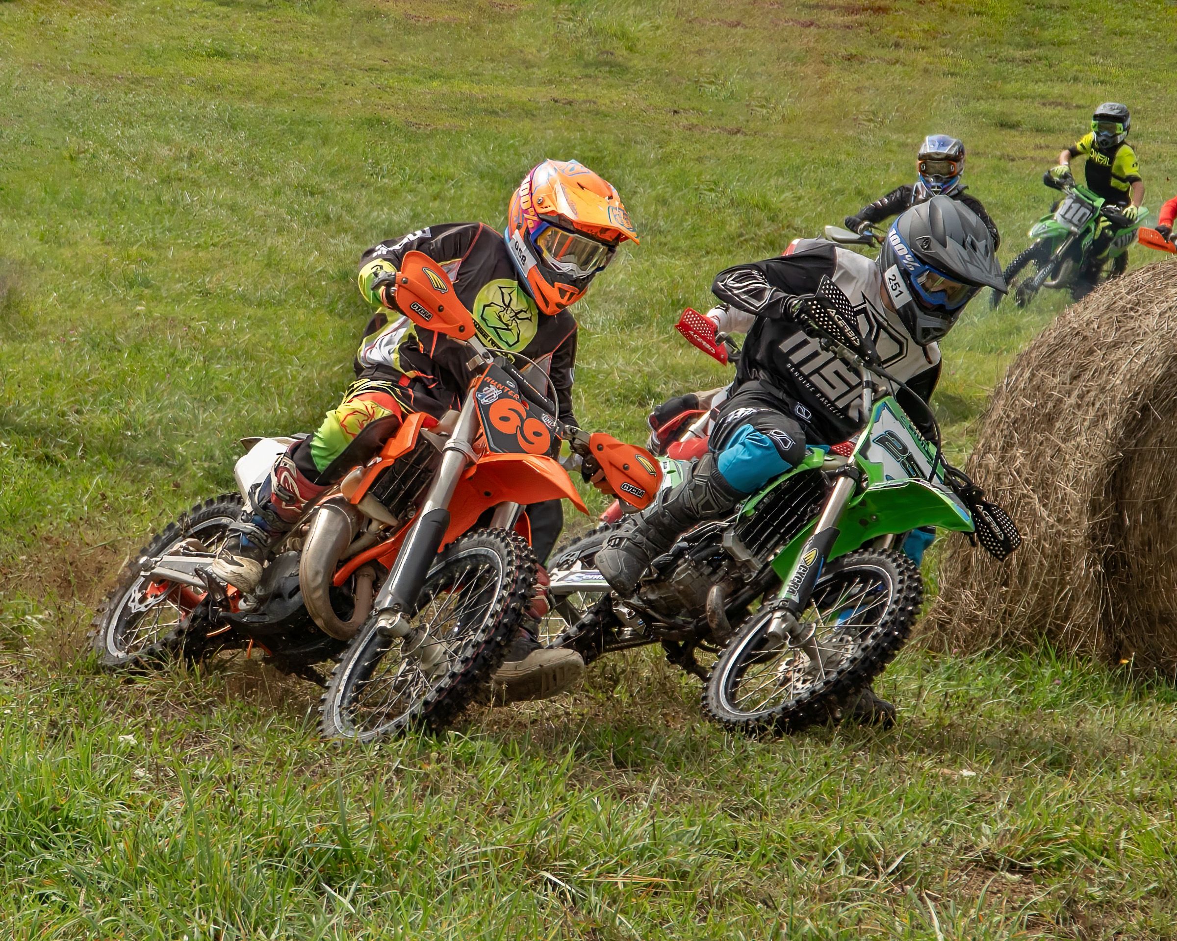 Several dirt bikes parked in a row on grassy terrain during what appears to be a motocross event.