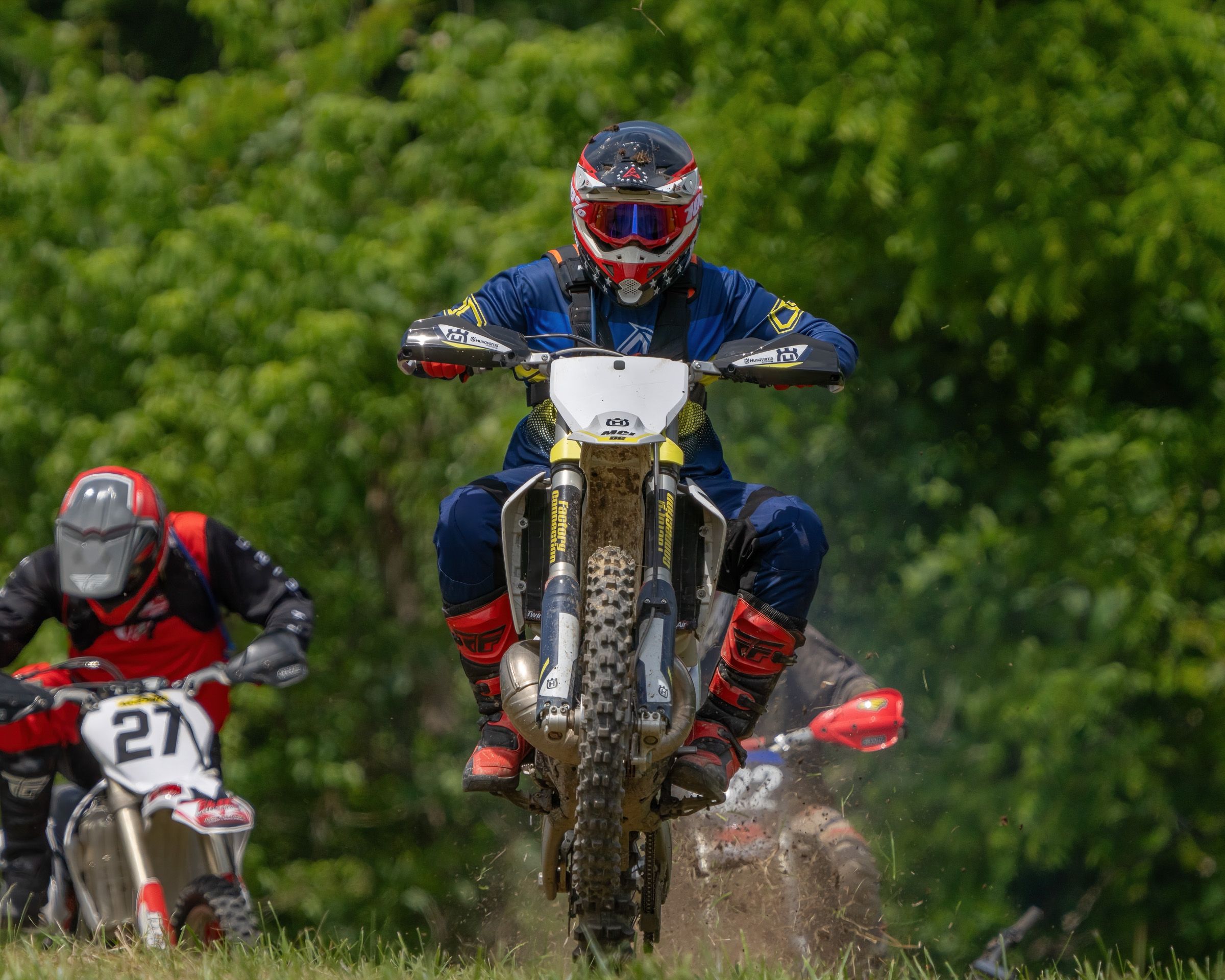 Motocross riders racing through muddy terrain with bikes kicking up dirt and debris during an intense competition.