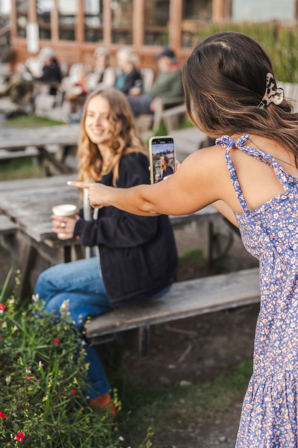 A person in a blue floral dress relaxes on a picnic bench near brick buildings on a sunny day.