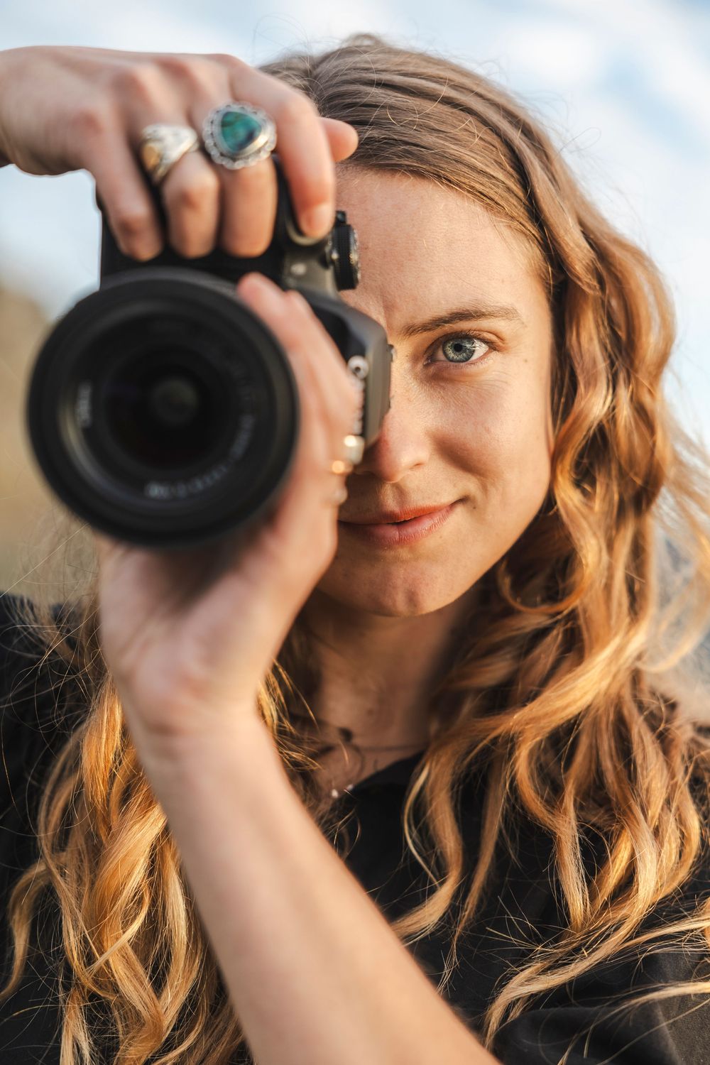 Close-up shots of photographer with wavy hair holding camera lens against dramatic sky background.