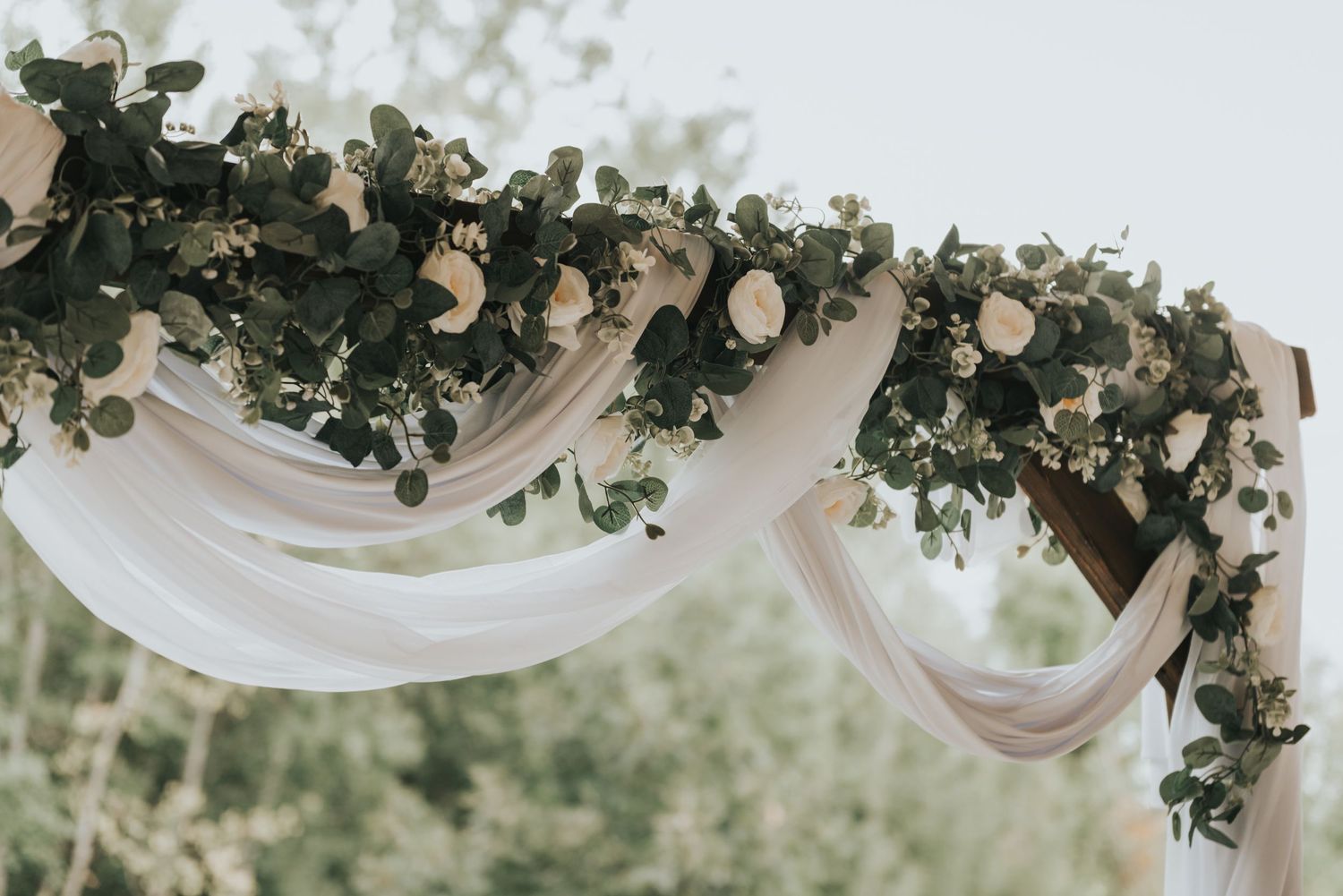 Elegant white fabric draping with eucalyptus garland creates a romantic wedding ceremony backdrop outdoors.
