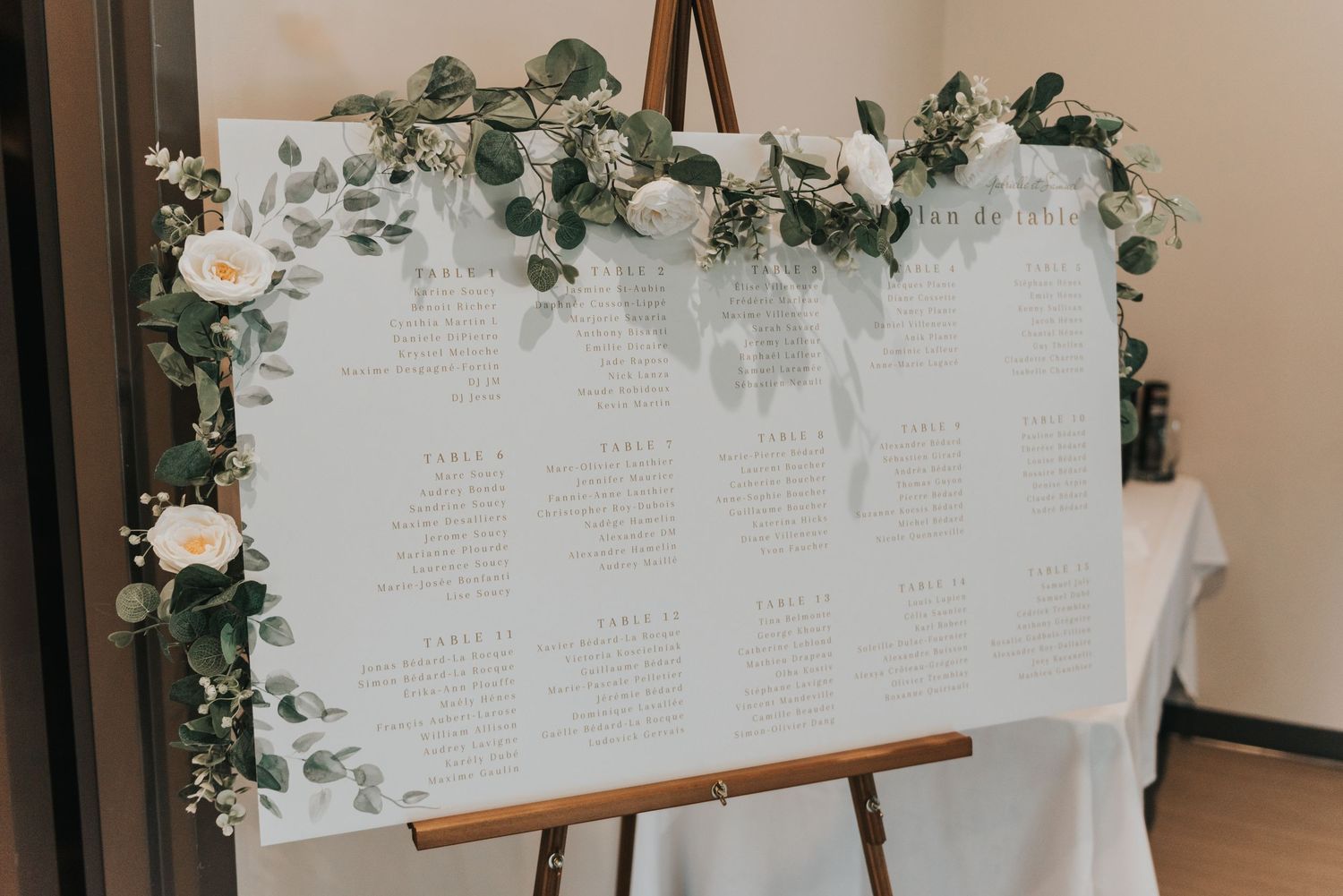 A white seating chart display board decorated with greenery and roses for an elegant wedding reception.