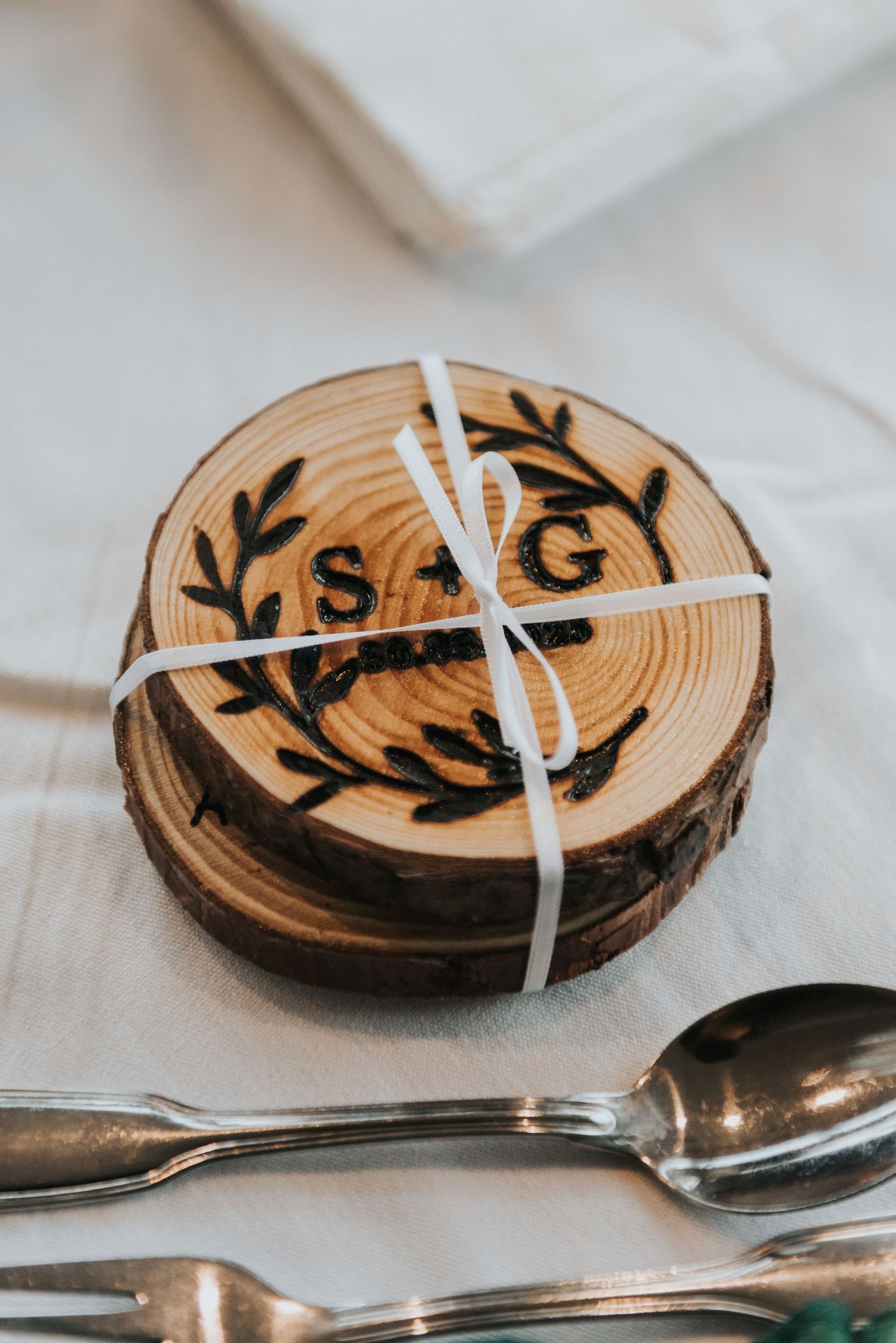 Rustic wooden log slice place cards with hand-painted initials and delicate white ribbon accents.