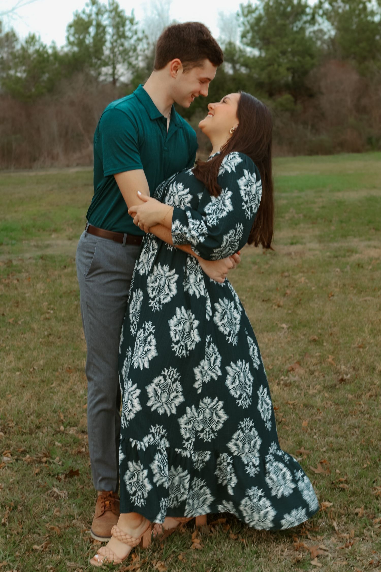 A couple in coordinating outfits share a romantic moment together in a grassy field on an overcast day.
