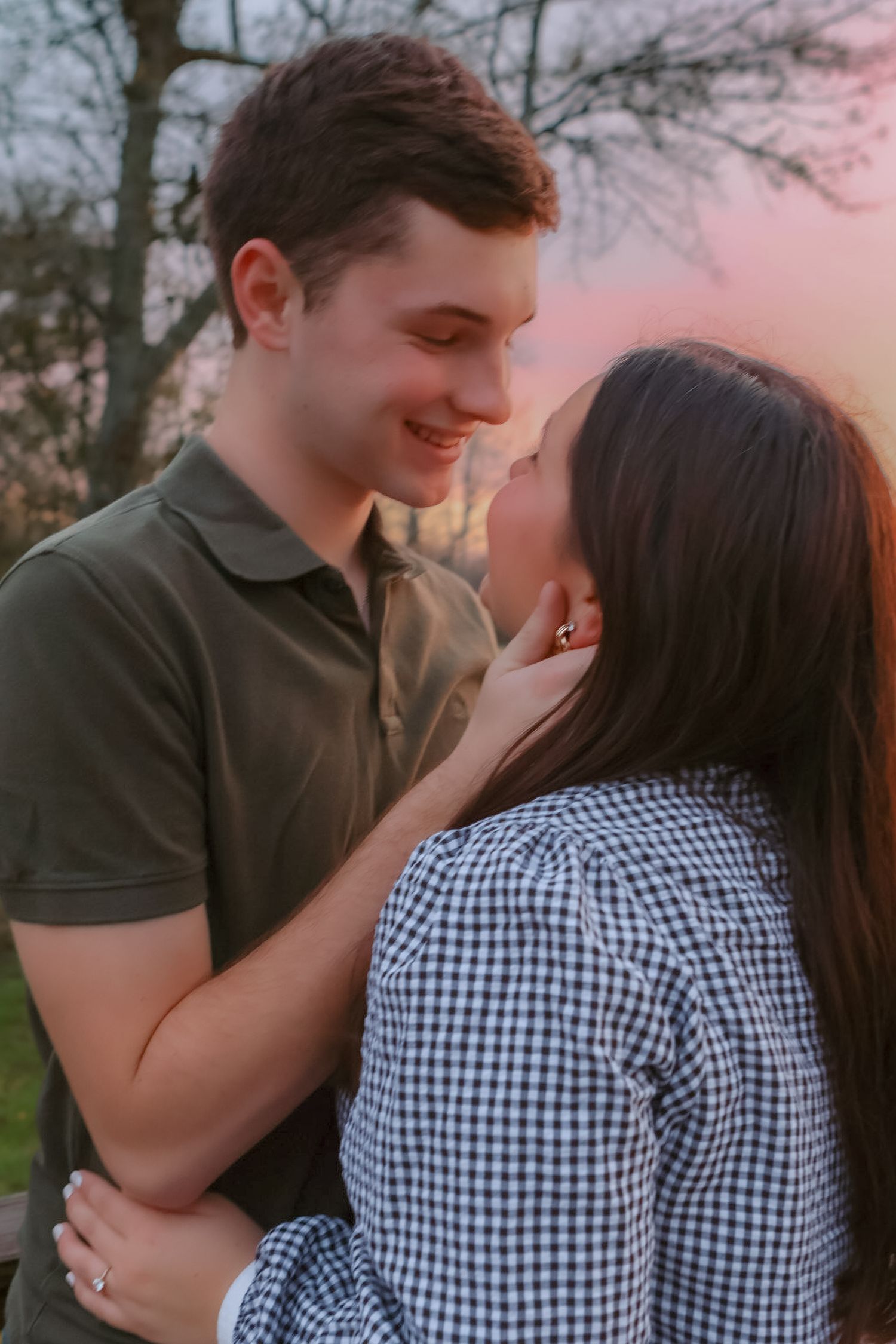 A couple shares an intimate moment outdoors at sunset wearing casual attire with a gingham print shirt.