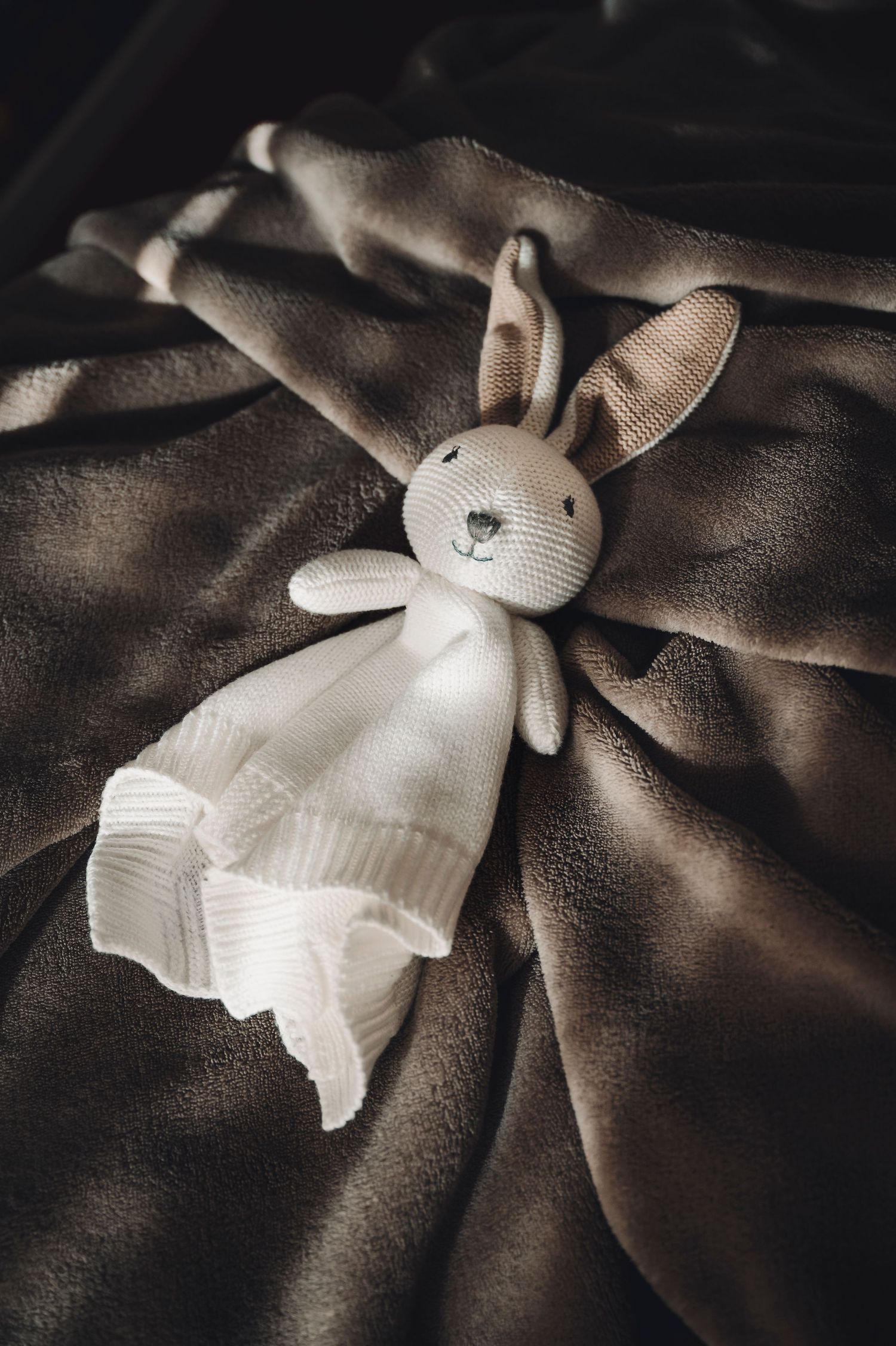 Coniglietto di peluche bianco lavorato a maglia sdraiato su un tessuto scuro con illuminazione drammatica.