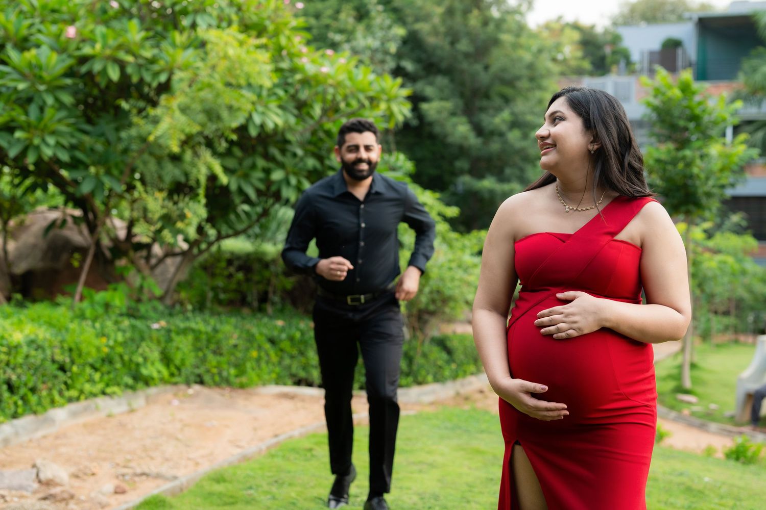 Couple walking together during outdoor maternity photoshoot, pregnant mother in red gown in Hyderabad