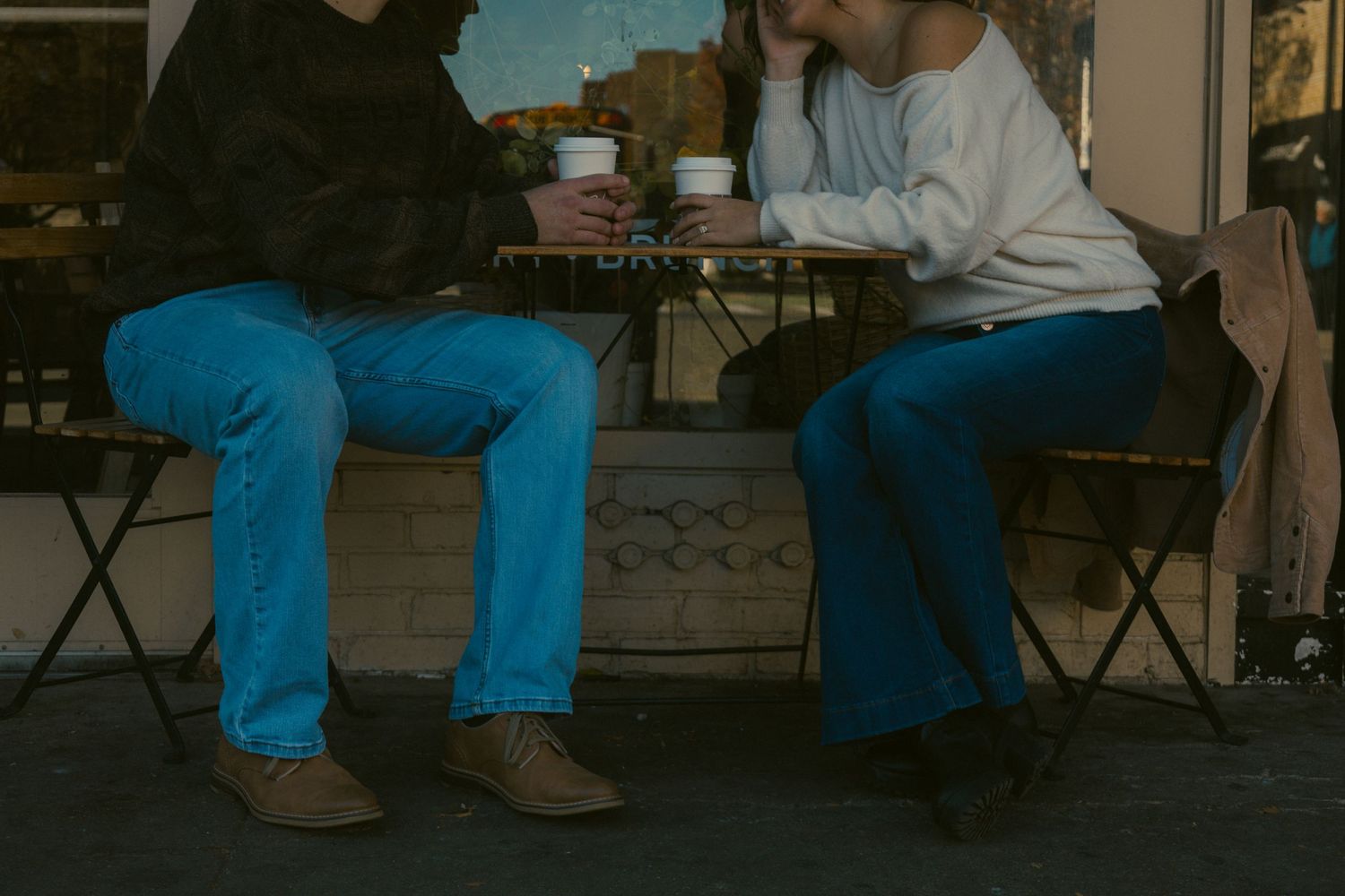 Two people share an intimate moment while sitting on chairs at a coffee shop in Ann Arbor Michigan during an engagement photo session.