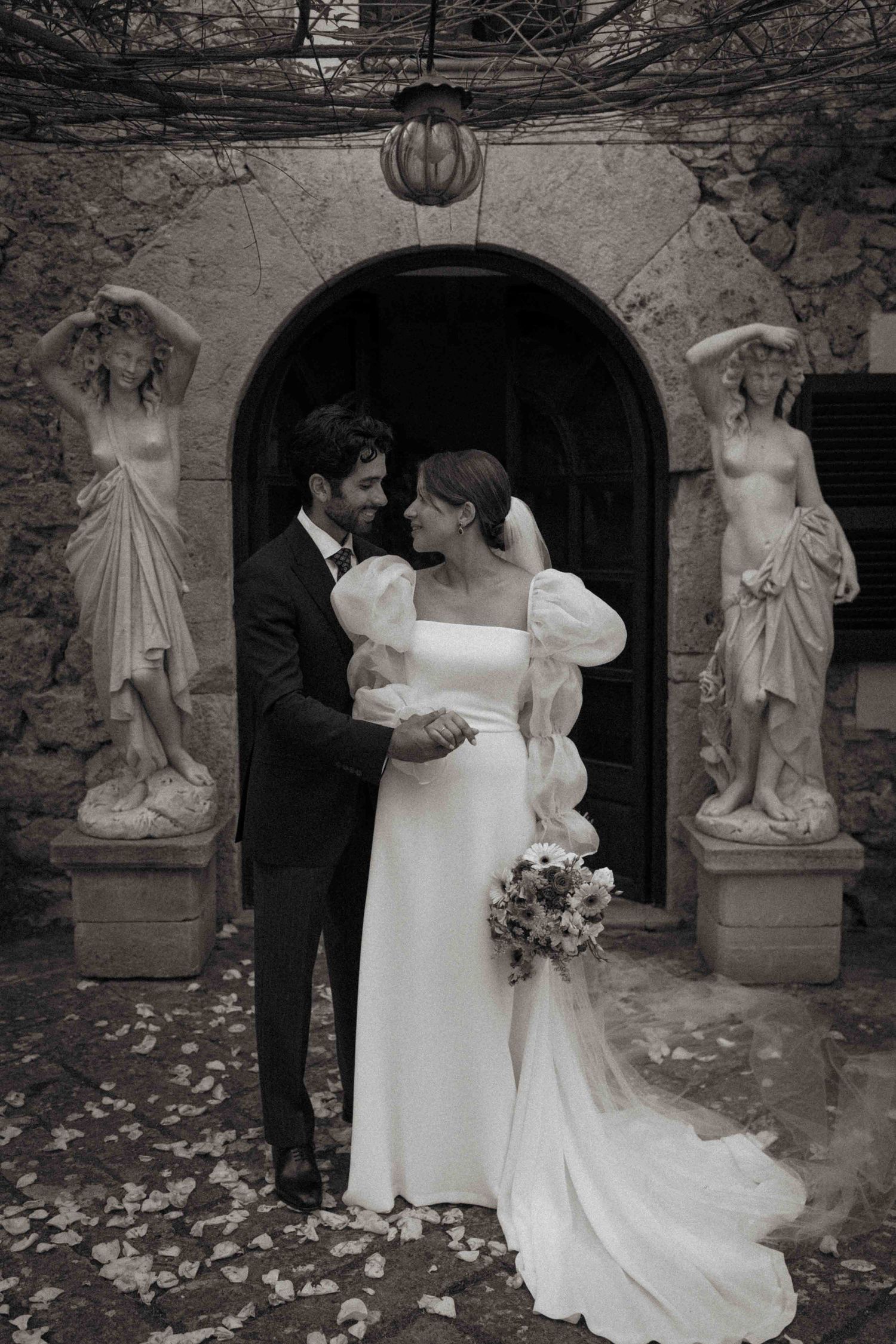 A romantic black and white wedding photo sequence showing a couple in formal attire embracing in a garden setting with statues.