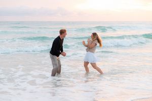 A couple splashes and plays together in the ocean waves during sunset at the beach.
