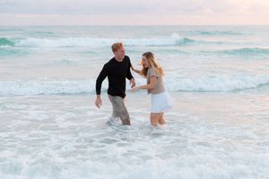 A couple playfully splashes in the ocean waves during sunset creating a romantic beach scene.