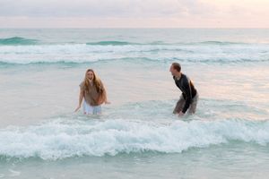 People swimming and playing in turquoise ocean waves during sunset at the beach.