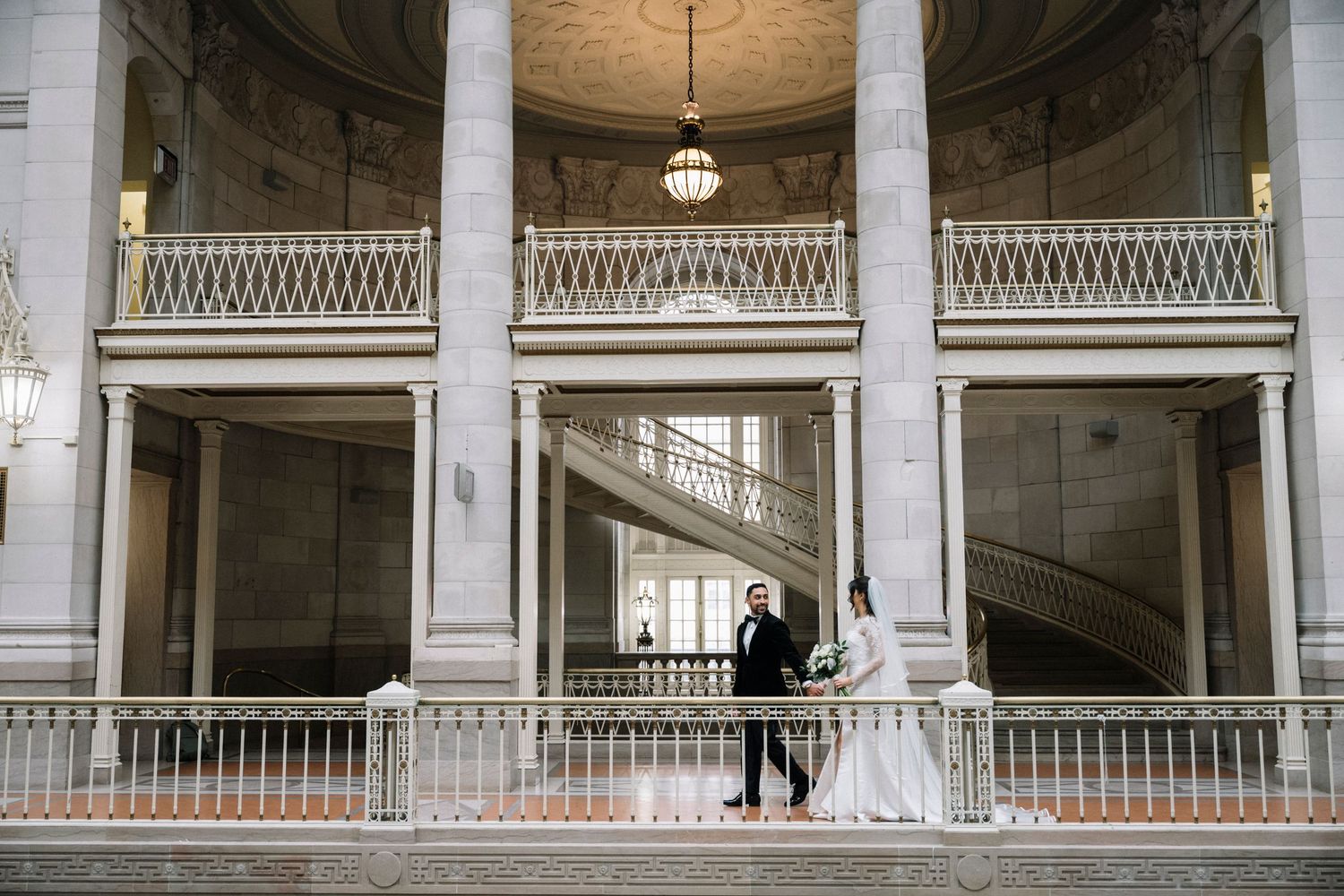 Classical interior architecture with white columns and balustrades featuring a silhouetted figure on a grand staircase.
