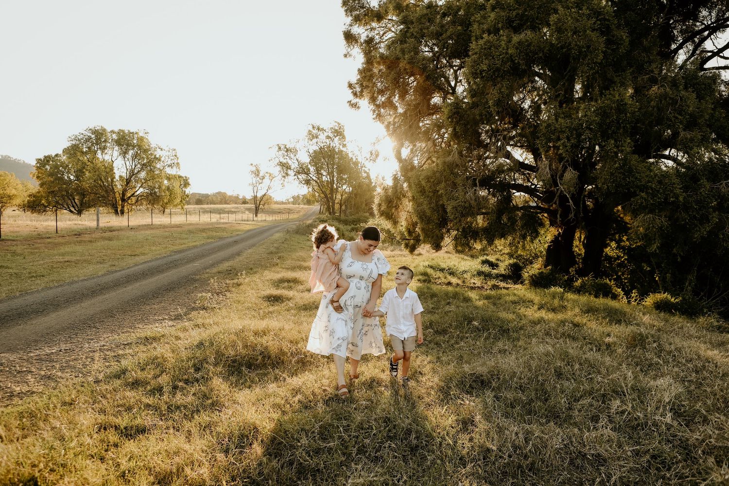 A family walks together in the sunset under a big shady tree
