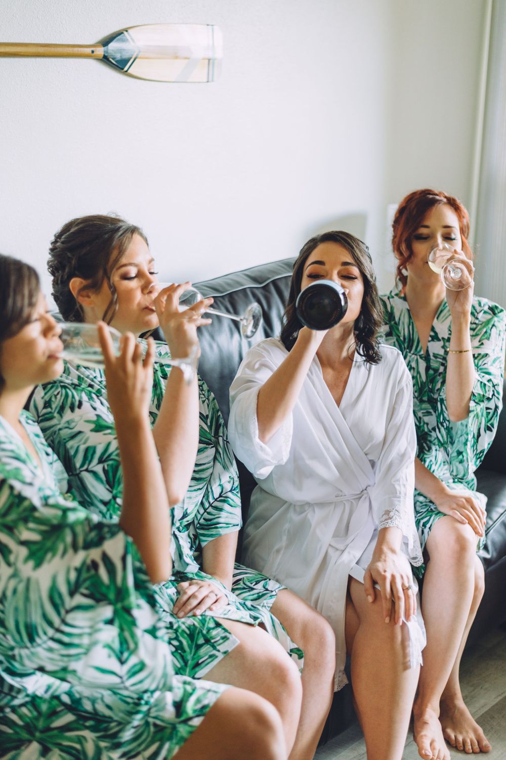 Group in matching green floral robes drinking champagne together on a sofa.