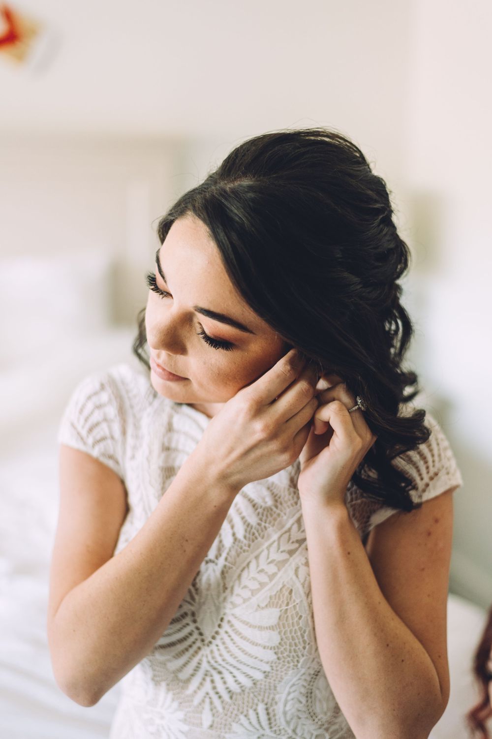 Side profile of someone putting on earrings while wearing a detailed lace dress.