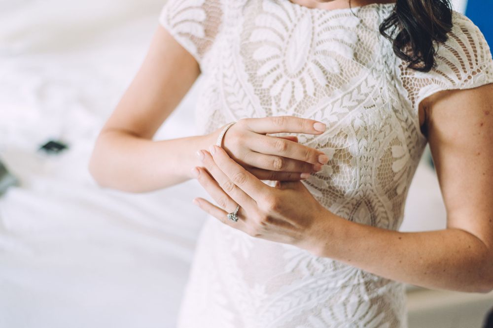 Close-up detail of hands touching intricate lace pattern on a white wedding dress.