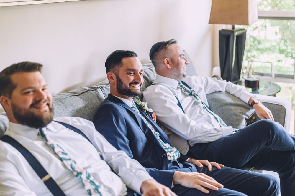 Wedding party members share a laugh while lounging on a gray sofa.