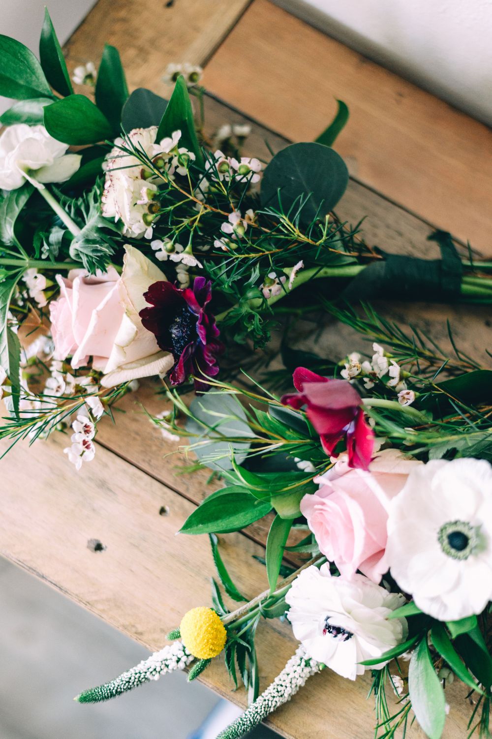 Fresh floral arrangement with pink roses, anemones and greenery laid on wooden surface.