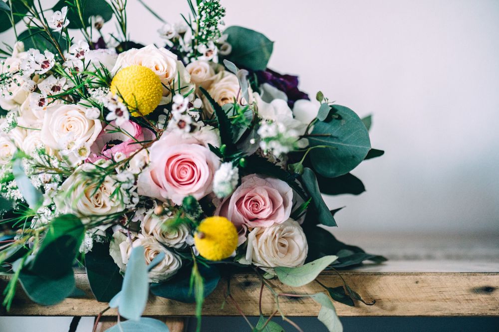 Romantic wedding bouquet with pink roses, yellow lemons, and eucalyptus on wooden surface.
