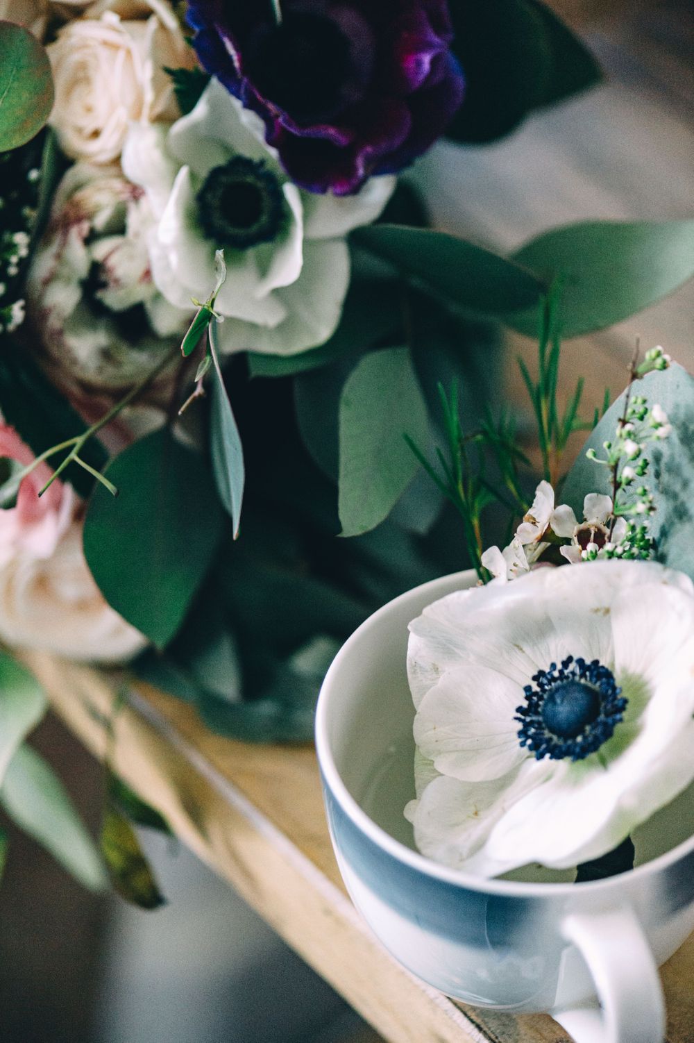 Close-up of white anemone flowers and greenery in a delicate teacup arrangement.