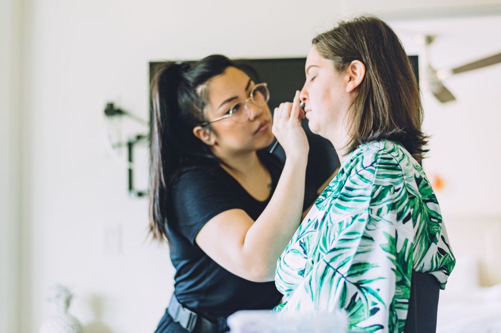 Makeup artist applying cosmetics on someone wearing a green tropical print robe.