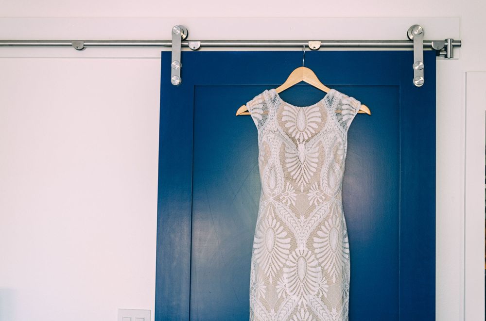 Elegant white lace wedding dress hanging against navy blue sliding door.