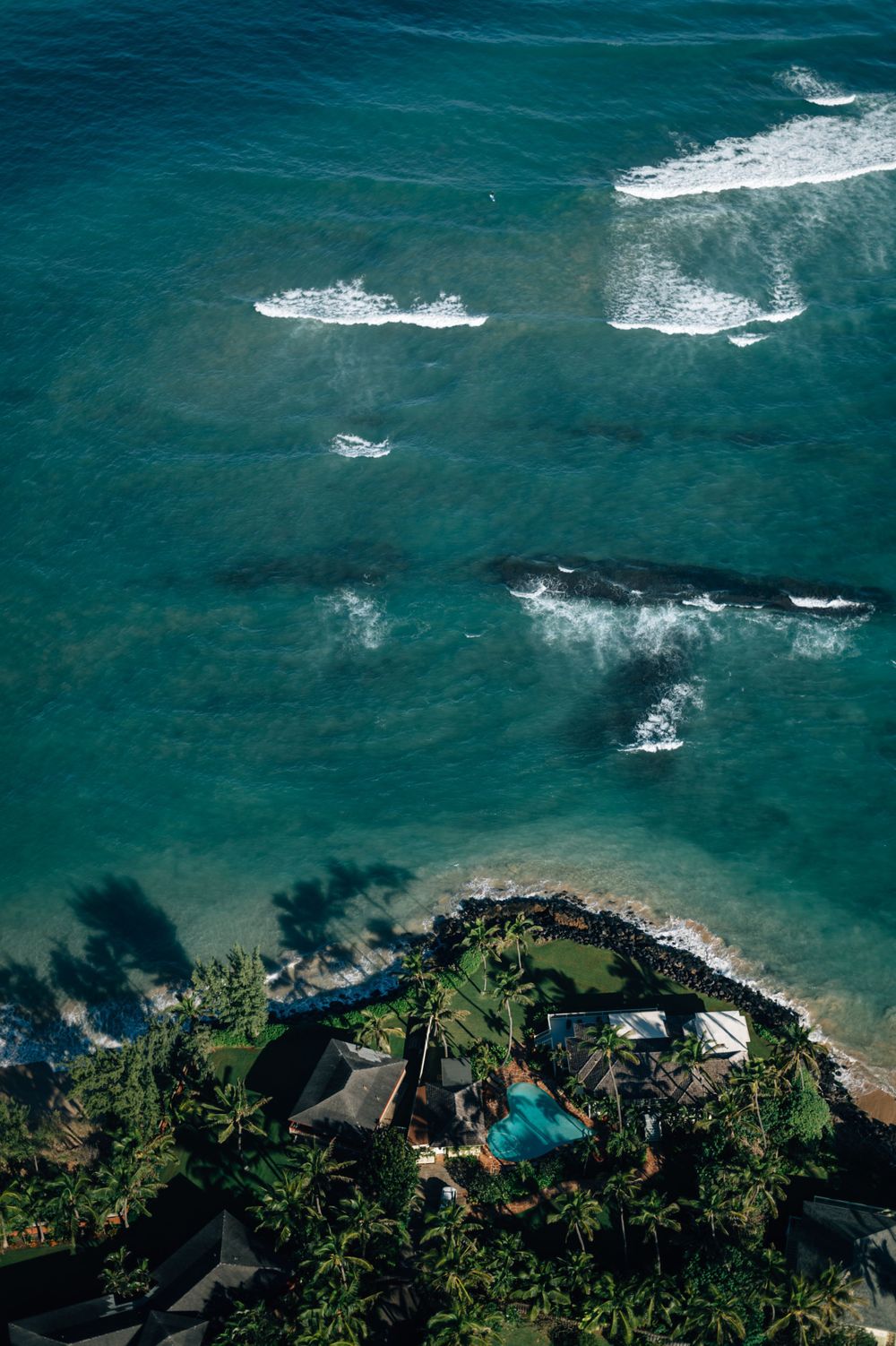 Aerial view of a luxury beachfront resort with swimming pool nestled among palm trees on turquoise waters.