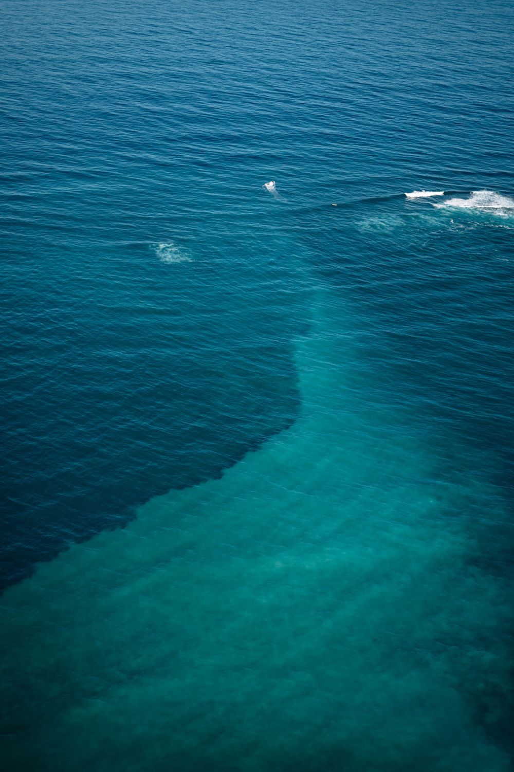Deep blue and turquoise ocean waters meeting with white wave breaks visible from above.