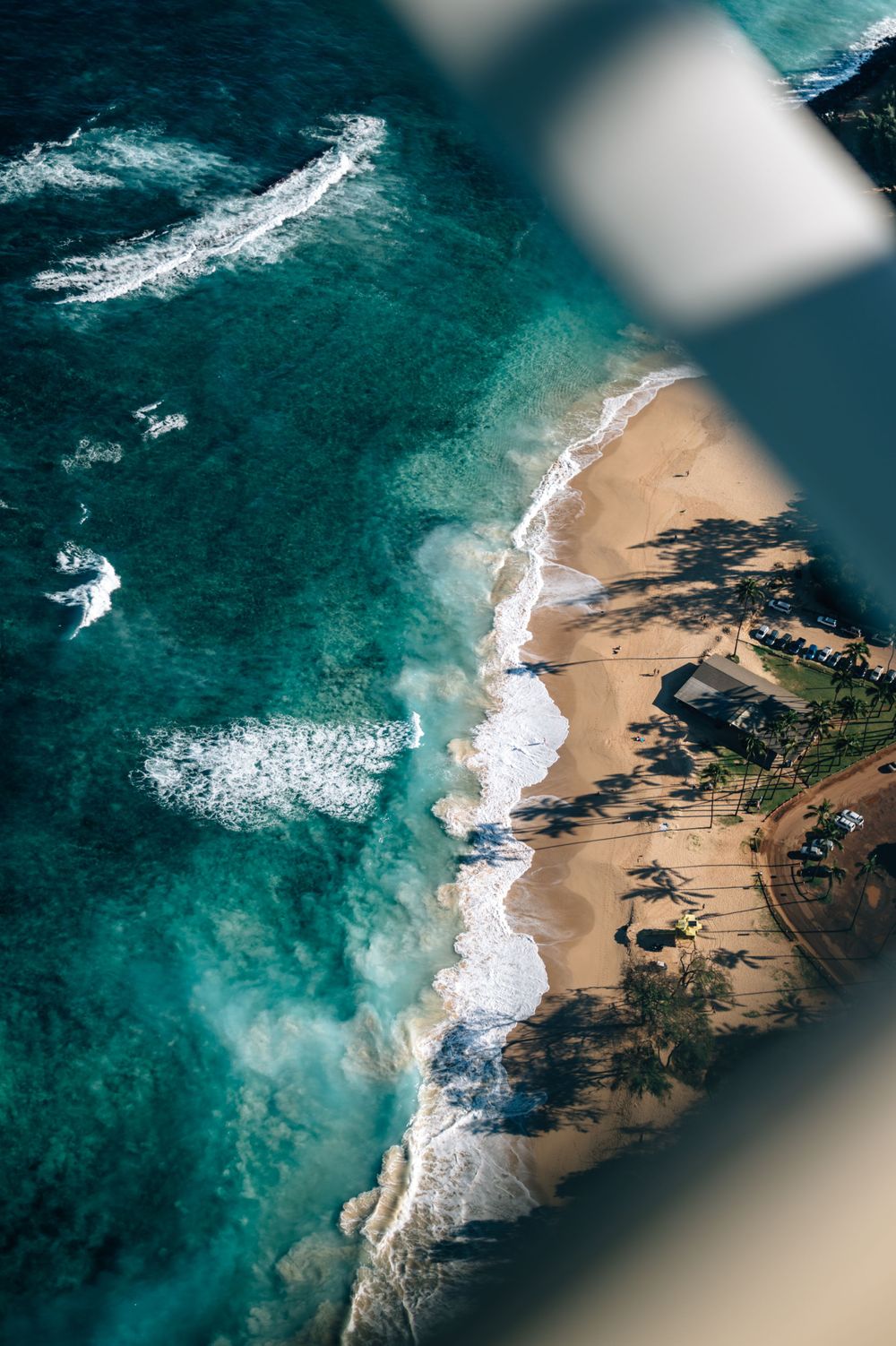 Aerial view of a sandy beach with crashing waves and rocky outcrops against turquoise ocean waters.