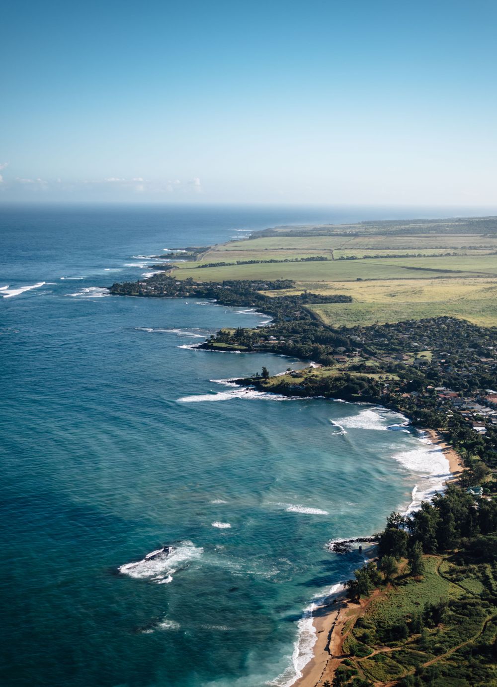 Coastal landscape showing rugged shoreline, farmland, and pristine beaches along turquoise waters.