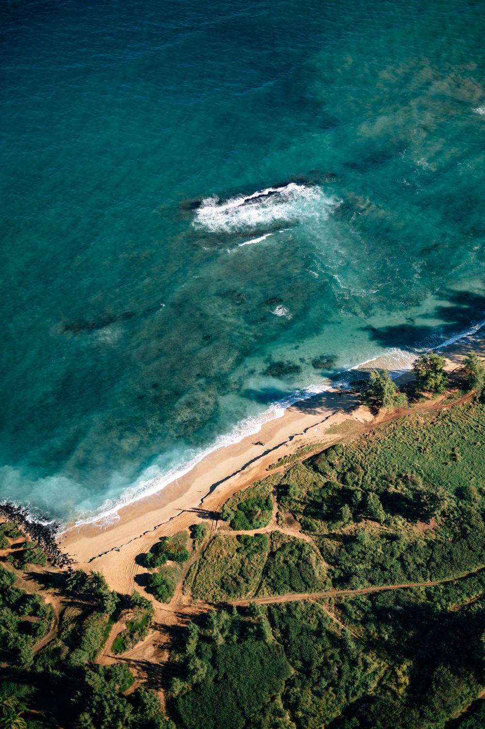 Curved beach cove with turquoise waters and winding coastal road viewed from above.