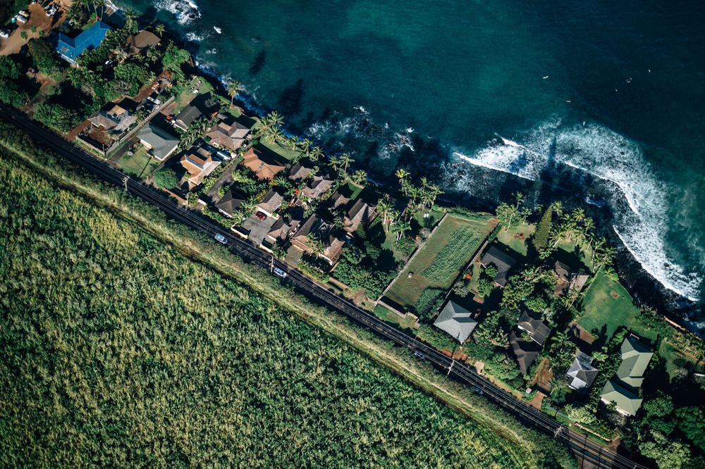 Aerial view of oceanfront residential properties with lush gardens along Hawaii's coastline.