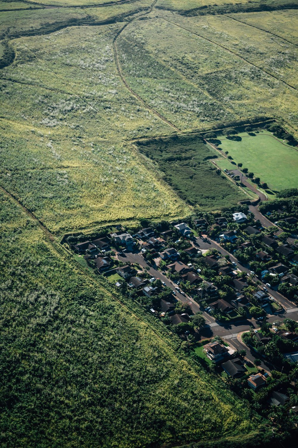 Aerial view of a residential development bordered by vast green fields and rolling hills.