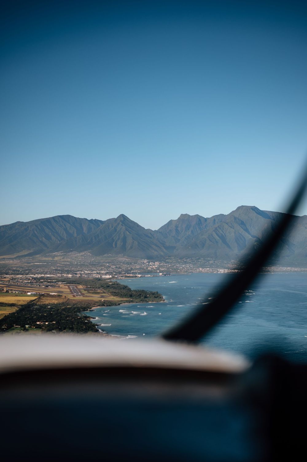 Mountain range and coastline viewed through aircraft window with dramatic blue skies.