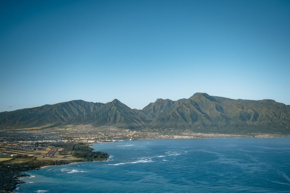 Panoramic view of a mountainous coastline with blue waters and rugged terrain.