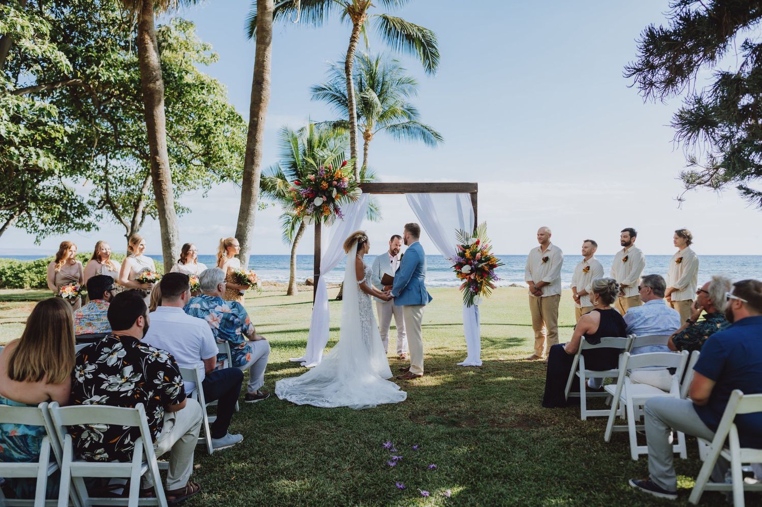 Beachfront wedding ceremony setup with white chairs and palm trees.