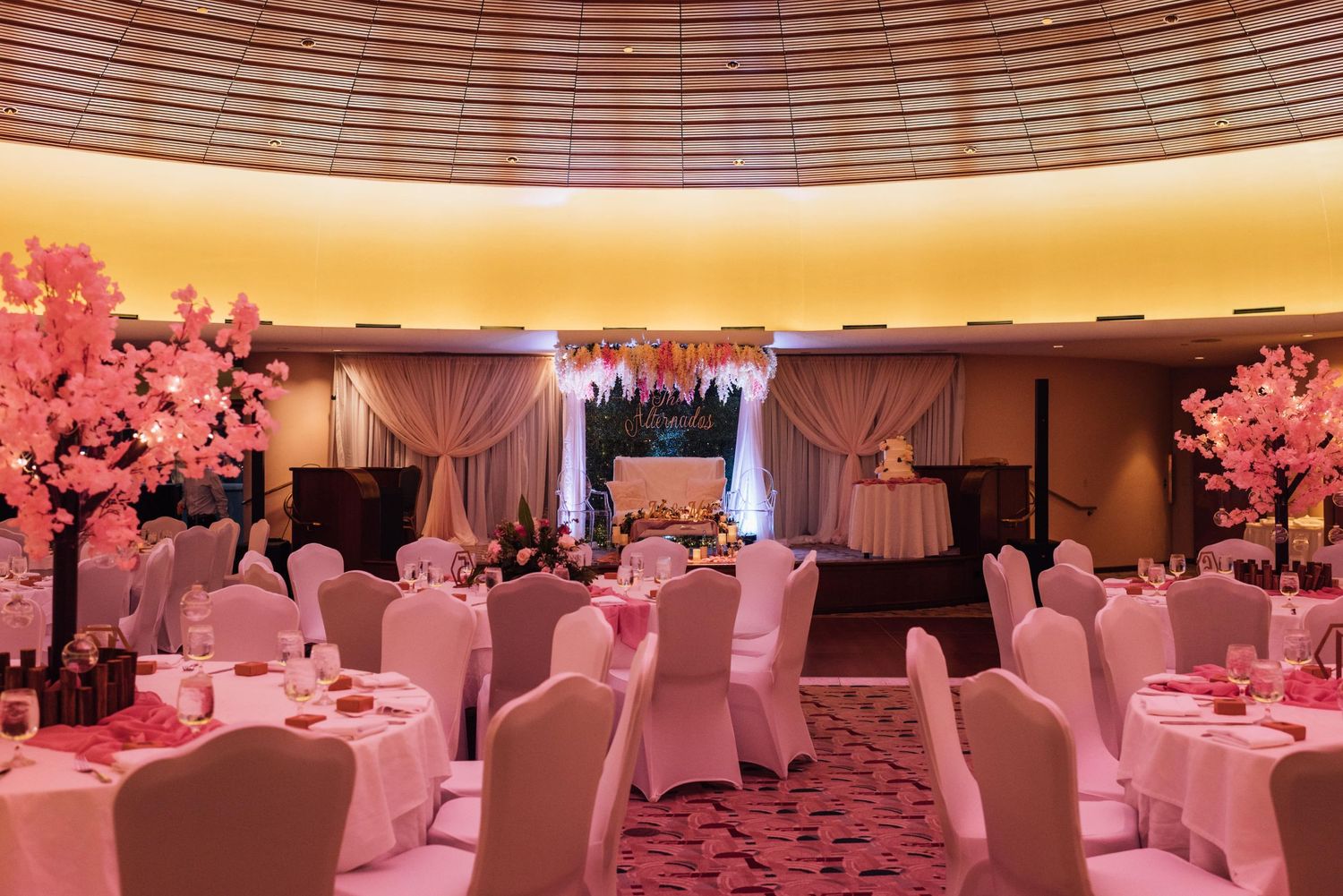 Elegant wedding reception ballroom with pink lighting and white table settings.