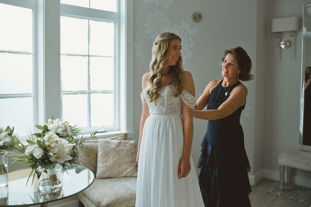 A bride in a white lace dress shares intimate moments with her wedding party in a bright sunlit room.