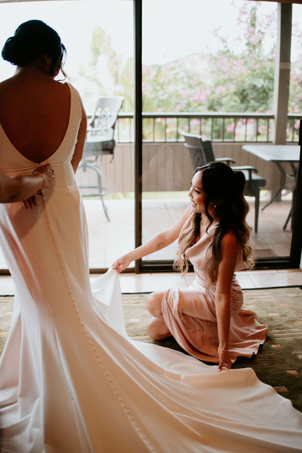 A wedding dress fitting scene shows a flowing white gown with buttons being adjusted in a sunlit room.