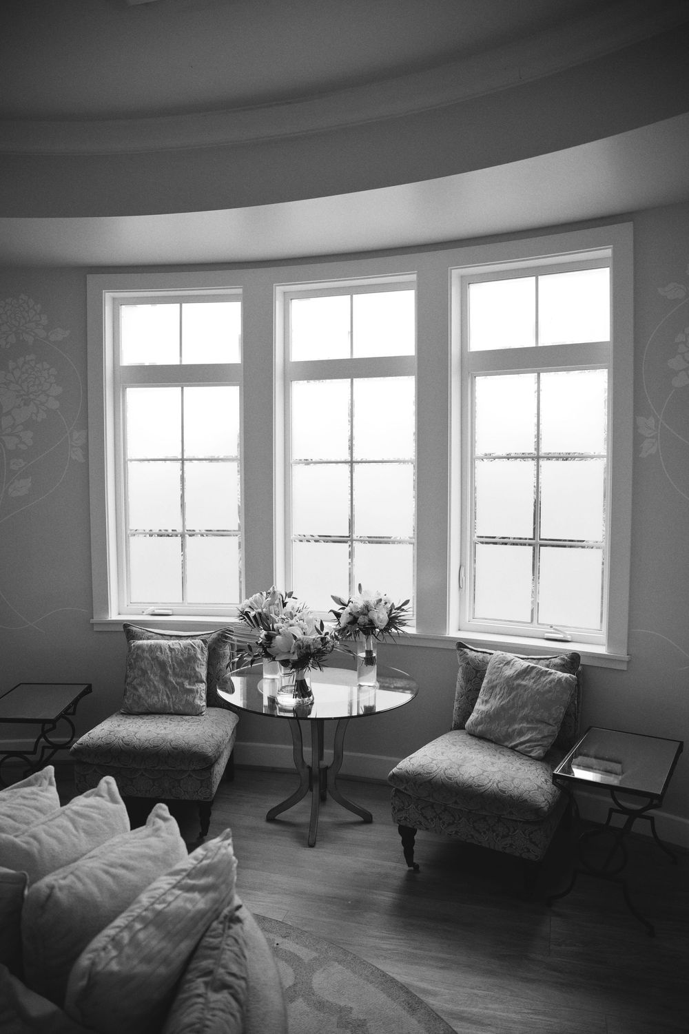 A modern room with bay windows, hardwood floors, and minimal furniture in black and white tones.
