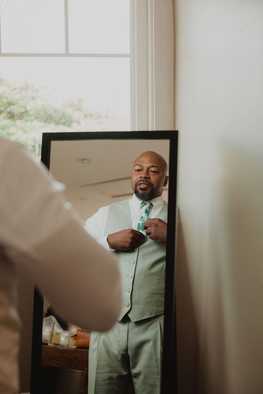 A sequence of four photos showing a person in a mint green suit adjusting their tie in a mirror.