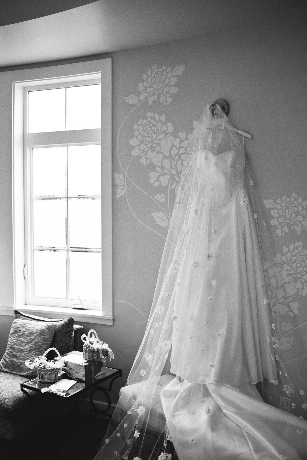 A series of black and white photographs showing a wedding dress and veil displayed against floral wallpaper near windows.