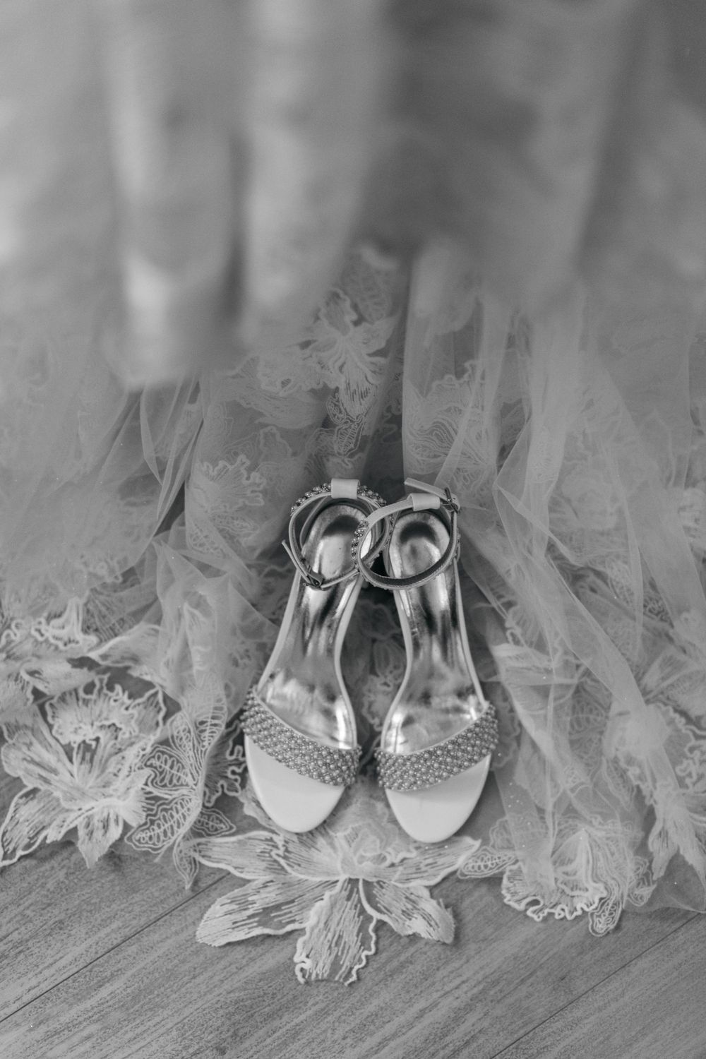 Elegant white bridal shoes arranged with delicate lace fabric in a soft black and white composition.