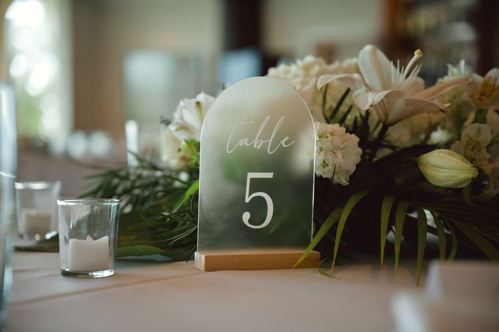 Elegant wedding table settings with frosted glass table numbers and white floral centerpieces create a romantic atmosphere.