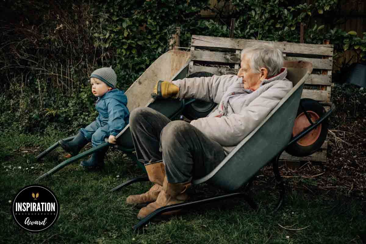 A grandfather holds a wheelbarrow still for hid grandson to sit inside while they enjoy a rest after gardening in Marlow.